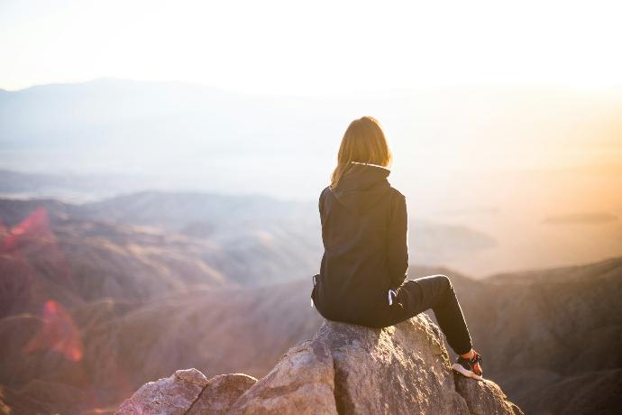 Person sitzt auf grauem Felsen mit Blick auf Berglandschaft bei Tageslicht.