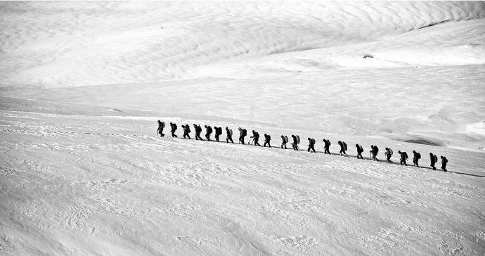 Der schneebedeckte Berg K2, der zweithöchste Berg der Welt, mit einer Gruppe, die gemeinsam den steilen Aufstieg bewältigen - Symbol für Teamarbeit und Zusammenhalt.