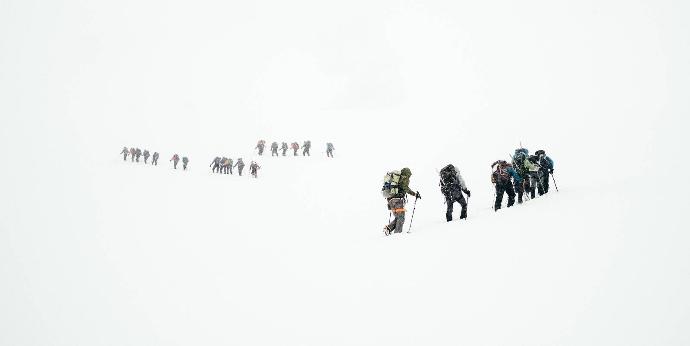 Der schneebedeckte Berg K2, der zweithöchste Berg der Welt, mit drei Gruppen, die gemeinsam den steilen Aufstieg bewältigen - Symbol für Teamarbeit und Zusammenhalt.